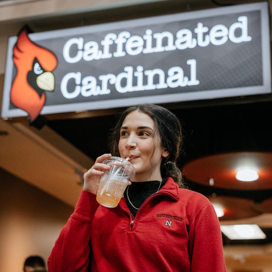 Student having a beverage in front of Caffeinated Cardinal sign